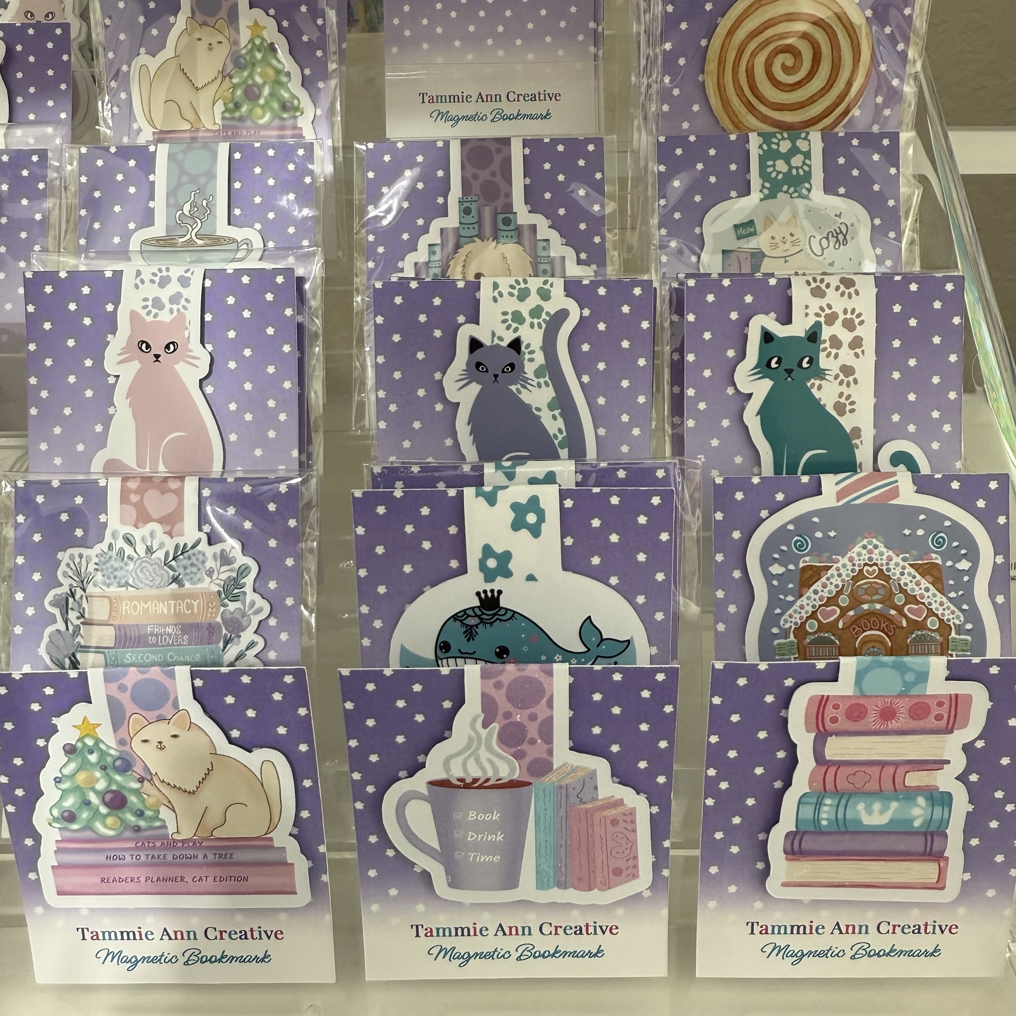 Display of various colorful cat-themed magnetic bookmarks with whimsical designs, arranged on a purple background.